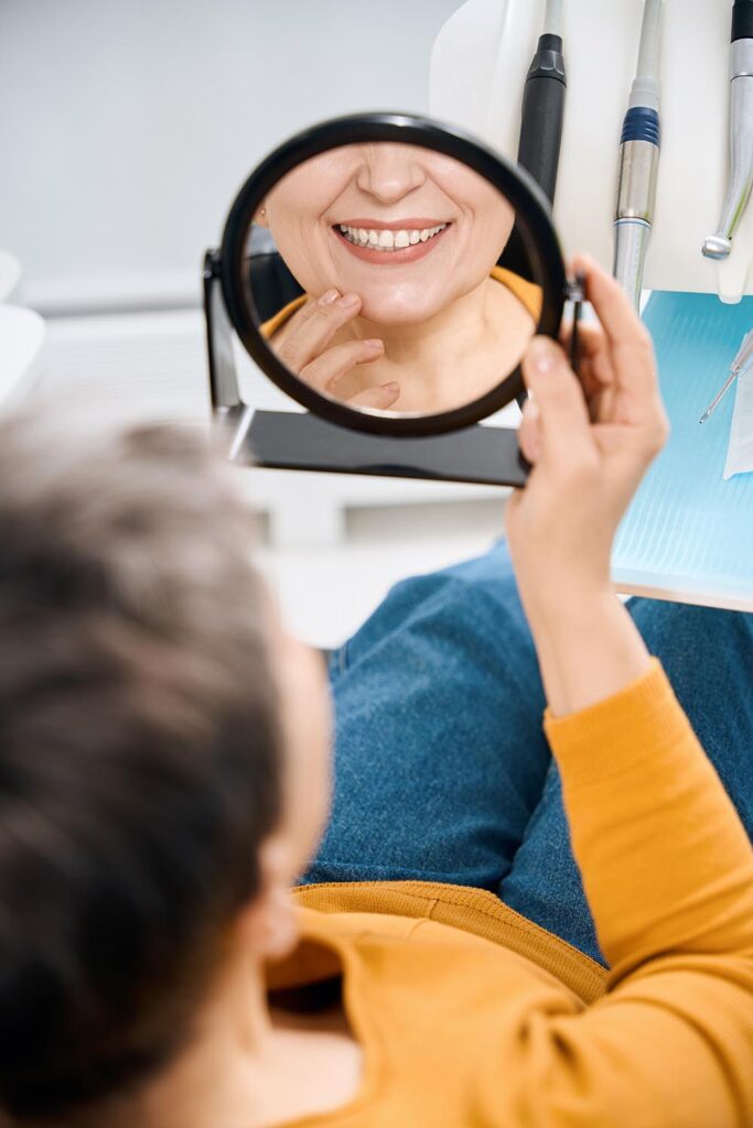 Patient smiling in a hand mirror after receiving comprehensive family dental care near Pinckney, MI.