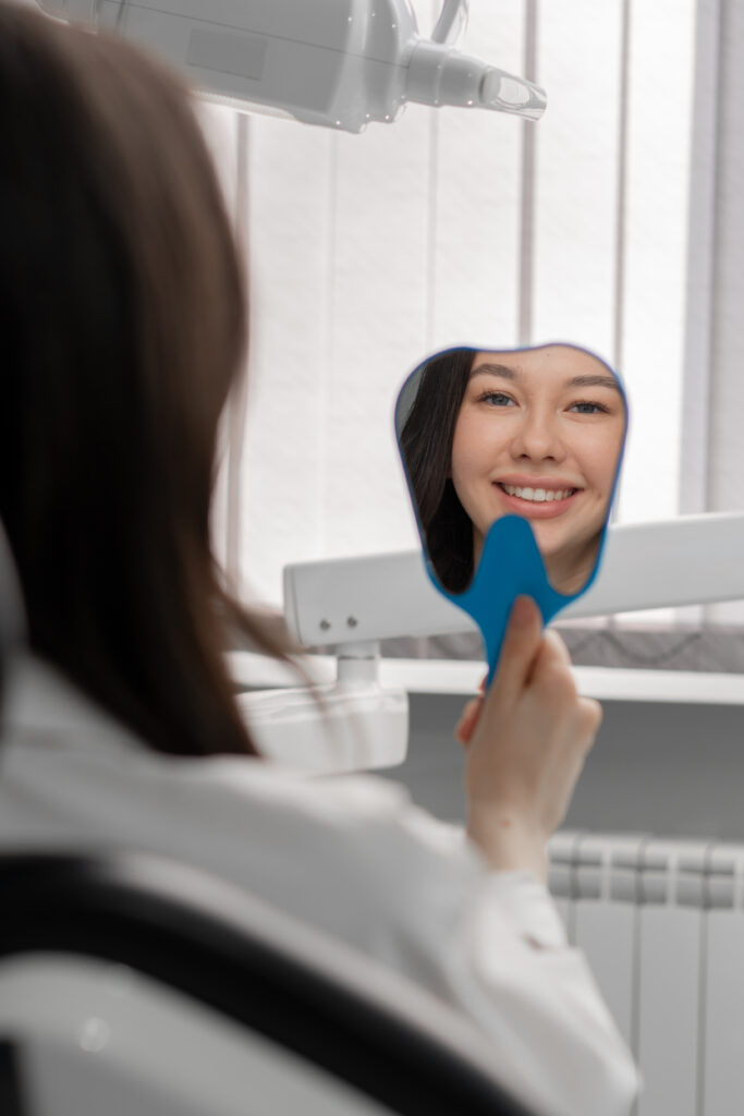 A dental patient admiring her bright, confident smile in a hand mirror during a visit to our dental practice serving Dexter.